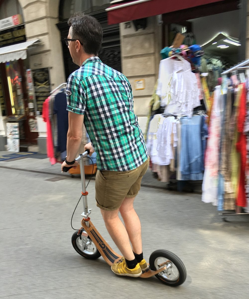man riding a boardy scooter through the city, demonstrating its low deck and smooth, surfing-like motion.