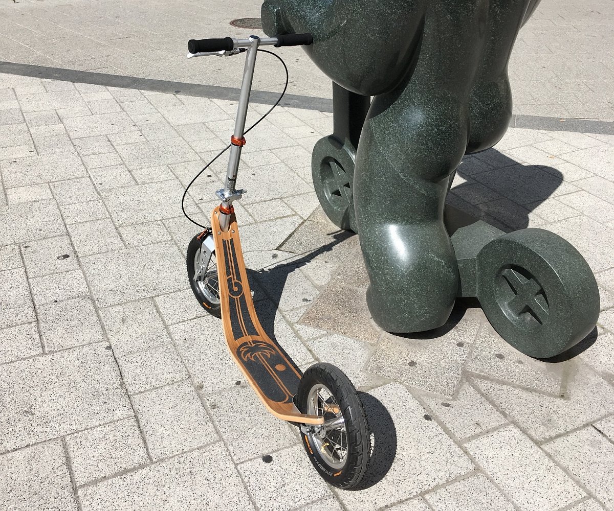 the classic model of boardy scooter parked next to a modern sculpture, showcasing its unique bamboo design.