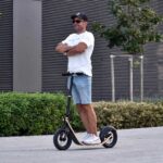Man confidently standing upright on a Boardy scooter with arms crossed, demonstrating its low center of gravity and wheel trail stability.