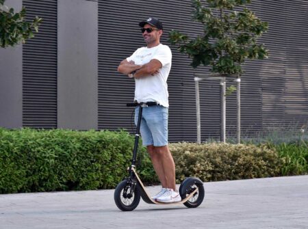 man confidently standing upright on a boardy scooter with arms crossed, demonstrating its low center of gravity and wheel trail stability.