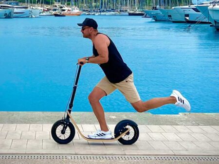 boardy rider pushing a human-powered boardscooter along a marina promenade, showing non-electric motion and big wheels.