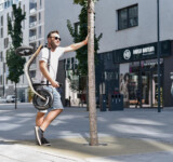 Take It With You a man holding a folded boardy and leaning against a tree