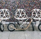 Intermission three boardy adult scooters parked folded against a mosaic-tiled wall, aligned beneath geometric white chairs.