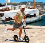 Smooth Moves At The Marina man pushing off on a boardy - the fastest kickscooter - in front of luxury yachts at a marina.