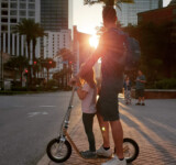 Family Moments On Boardy adult and child standing together on a boardy kick scooter at sunset in an urban setting.