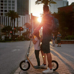 Family Moments On Boardy adult and child standing together on a boardy kick scooter at sunset in an urban setting.