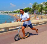 Effortless Coastal Cruising man riding a boardy kick scooter along a sunny seaside promenade.