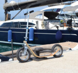 Dockside Companion boardy scooter parked next to a luxury yacht in a marina.