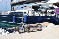 Dockside Companion boardy scooter parked next to a luxury yacht in a marina.