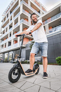 Sleek Urban Ride man standing on a boardy scooter in front of a modern urban building.