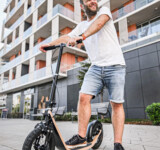 Sleek Urban Ride man standing on a boardy scooter in front of a modern urban building.