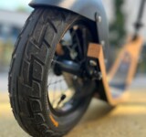 Precision Grip. Built To Roll. close-up of boardy’s back wheel on a paved surface, showing tire tread and deck detail.