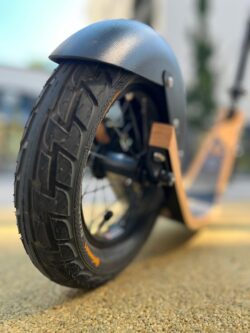 Precision Grip. Built To Roll. close-up of boardy’s back wheel on a paved surface, showing tire tread and deck detail.