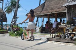 Tropical Ride Vibes woman riding a boardy scooter in a tropical resort area near bungalows.