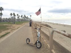 Freedom On Two Wheels boardy scooter on a path beside the ocean with an american flag in the background.