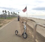 Freedom On Two Wheels boardy scooter on a path beside the ocean with an american flag in the background.