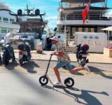 Dockside Ride rider near a jacht with a boardy scooter on a dock.