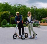 Park Pause two riders with boardy scooters chatting in a park.