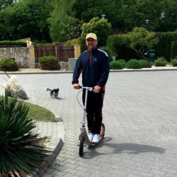 Leisurely Stroll majka pushing a boardy scooter on a paved park path.