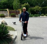 Leisurely Stroll majka pushing a boardy scooter on a paved park path.