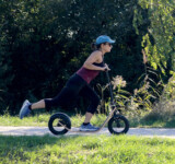 Great For Cardio young woman riding a boardy scooter across a sunny grassy field.