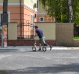 Rolling Rehabilitation man with a prosthetic leg riding a boardy scooter across a city street.