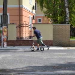 Rolling Rehabilitation man with a prosthetic leg riding a boardy scooter across a city street.